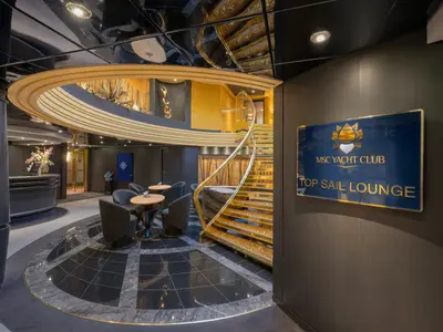 Elegante Top Sail Lounge des MSC Yacht Clubs an Bord der MSC Preziosa. Eine goldene Wendeltreppe, Rezeption und stilvolle Sitzbereiche prägen das luxuriöse Ambiente.