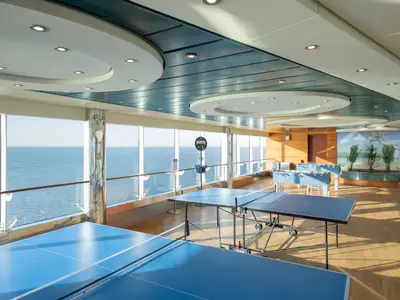 Ein heller Freizeitbereich an Bord der MSC Preziosa mit blauen Tischtennisplatten und Kickertischen vor großen Panoramafenstern mit Meerblick.