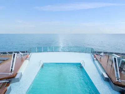 Blick auf den Garden Pool am Heck der MSC Preziosa. Von Holzdecks umgebene Heckpools mit Meerblick und blauem Himmel am Horizont.