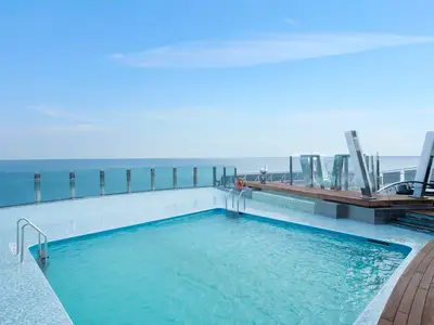 Ein weitläufiger Swimmingpool auf dem Sonnendeck der MSC Preziosa. Mit Glasgeländer und Holzboden bietet der Poolbereich einen weiten Meerblick unter strahlend blauem Himmel.