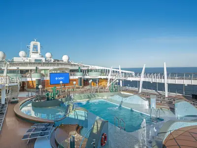 Blick auf den weitläufigen Poolbereich der MSC Preziosa mit mehreren Pools und Whirlpools an Deck. Im Hintergrund ist das offene Meer und ein grosser LED-Bildschirm zu sehen, der das MSC Logo anzeigt.