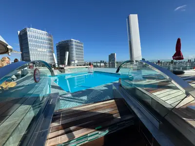 Ein einladender, blauer Pool auf dem Außendeck an Bord der MSC Preziosa vor einer modernen City-Skyline.