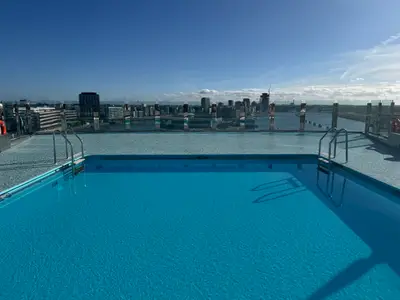 Blick über den blauen Pool an Bord der MSC Preziosa auf eine Stadt-Skyline bei klarem Tageslicht.