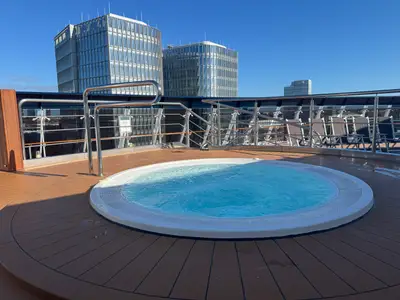 Ein sprudelnder runder Whirlpool auf dem Außendeck an Bord der MSC Preziosa vor der Kulisse moderner Hochhäuser.