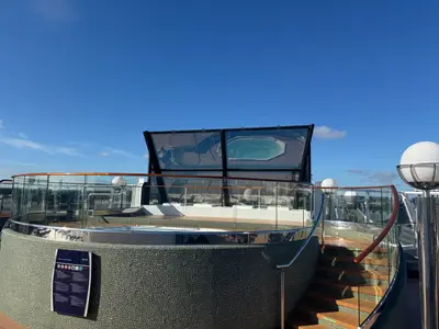 Ein moderner Whirlpool mit Mosaiksteinverkleidung und Glasschutzwand an Bord der MSC Preziosa unter blauem Himmel.
