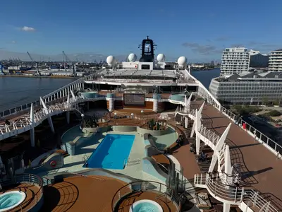 Blick von oben auf das moderne Pooldeck an Bord der MSC Preziosa mit einem blauen Pool, Liegestühlen und Hafenpanorama im Hintergrund.