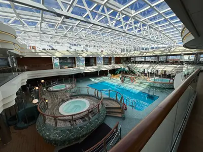 Der lichtdurchflutete, überdachte Poolbereich an Bord der MSC Preziosa mit einem Hauptbecken, mehreren Whirlpools und einem großen Glasdach.
