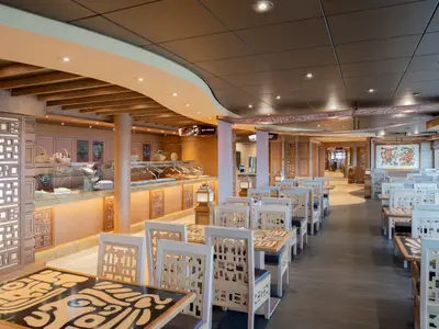 Ansicht des Inca & Maya Buffet-Restaurants an Bord der MSC Preziosa. Ein warmer Innenraum mit Essensstationen, Holzelementen und zahlreichen Tischen und Stühlen für Gäste.