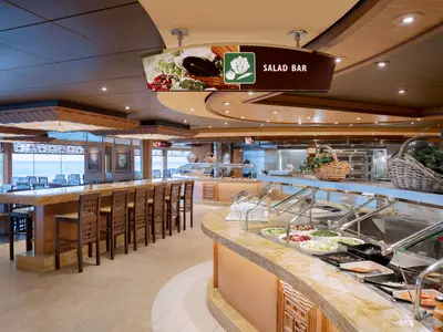 Das helle Buffetrestaurant der MSC Preziosa zeigt eine lange Salatbar mit frischen Zutaten. Dahinter laden Tische und Stühle zu einem Essen mit Meerblick ein.