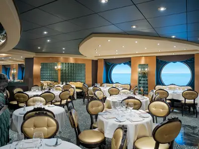 Das luxuriöse Restaurant 'The Golden Lobster' an Bord der MSC Preziosa. Festlich gedeckte Tische, goldene Stühle und grüne Sofas. Große Bullaugen bieten weiten Meerblick.