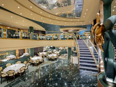 Das mehrstufige Restaurant 'The Golden Lobster' an Bord der MSC Preziosa. Zahlreiche gedeckte Tische, goldene Stühle, eine beleuchtete Treppe und eine goldene Skulptur.