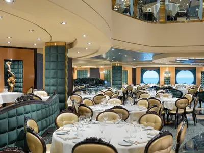 Elegantes Restaurant 'The Golden Lobster' an Bord der MSC Preziosa mit gedeckten Tischen, gold-grünen Stühlen und Wänden. Große Bullaugen bieten Meerblick.