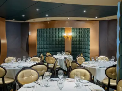 Elegantes Restaurant an Bord der MSC Preziosa. Gedeckte Tische mit goldenen Stühlen. Grüne, gepolsterte Wände und eine goldene Wandleuchte schaffen ein luxuriöses Ambiente. Innenraumansicht.