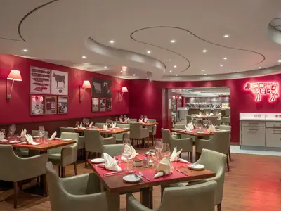 Das helle Spezialitätenrestaurant Butcher's Cut an Bord der MSC Preziosa zeigt rote Wände mit Rindfleisch-Motiven und viele gedeckte Tische.