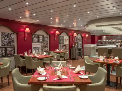 Ein stilvolles Spezialitätenrestaurant Butcher's Cut an Bord der MSC Preziosa. Die roten Wände sind mit gerahmten Bildern von Fleischschnitten und Farmmotiven dekoriert. Gedeckte Holztische mit hellen Stühlen laden zum Essen ein.