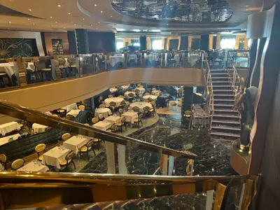 Blick auf das zweistöckige Hauptrestaurant an Bord der MSC Preziosa mit goldenen Geländern und elegant gedeckten Tischen.