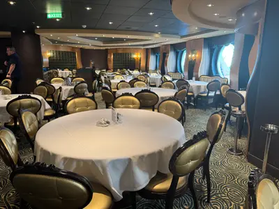 Das festliche Hauptrestaurant an Bord der MSC Preziosa mit runden, weiß gedeckten Tischen und goldenen Polstersesseln.