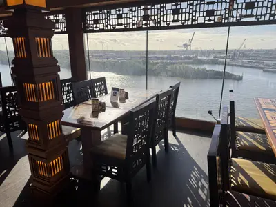 Blick durch das Panoramafenster eines asiatischen Restaurants an Bord der MSC Preziosa auf ein Hafengebiet.