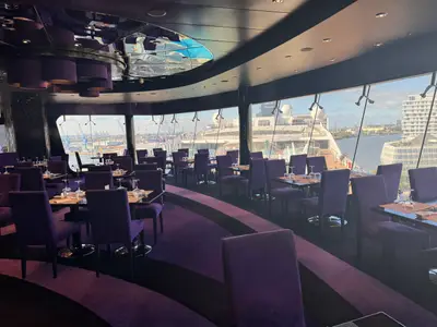 Blick aus dem eleganten Restaurant an Bord der MSC Preziosa durch große Fenster auf den Hafen und ein anderes Schiff.