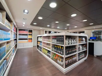 Ein heller, moderner Duty-Free-Shop an Bord der MSC Preziosa. Eine zentrale, geschwungene Theke präsentiert diverse Alkoholflaschen. Wandregale sind mit Tabakprodukten bestückt. Eine Kasse ist sichtbar.