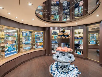 Ein heller, runder Shop an Bord der MSC Preziosa mit Glasvitrinen voller Souvenirs, Plueschtieren, Mützen und MSC-Logo-Artikeln.