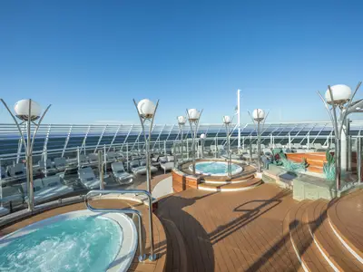 Blick auf das obere Sonnendeck der MSC Preziosa mit zwei sprudelnden Whirlpools, zahlreichen Liegen und modernen Leuchten unter strahlend blauem Himmel. Keine Personen sind sichtbar.
