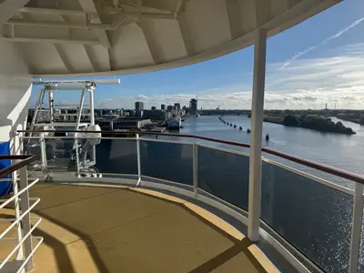 Blick von einem Außendeck der MSC Preziosa mit Glasreling auf einen Fluss und eine moderne Skyline unter blauem Himmel.