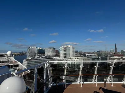 Blick von der Reling an Bord der MSC Preziosa auf die moderne Architektur der HafenCity in Hamburg unter blauem Himmel.