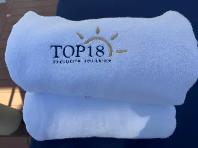 Nahaufnahme eines weißen Handtuchs mit gesticktem 'Top 18 Exclusive Solarium'-Logo an Bord der MSC Preziosa.