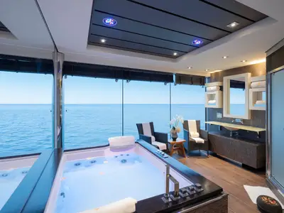 Luxuriöser Spa-Bereich mit beleuchtetem Jacuzzi und Blüten an Bord der MSC Preziosa. Die Glasfront erlaubt weiten Blick auf das Meer. Sitzgelegenheiten, Waschtisch und Dusche.