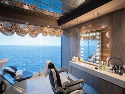 Barber Shop im MSC Aurea Spa der MSC Preziosa. Er zeigt Frisierstühle, Waschtisch und einen beleuchteten Spiegel. Meerblick durch Panoramafenster.