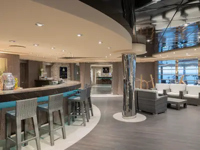 Moderne Bar und Lounge im MSC Aurea Spa an Bord der MSC Preziosa. Eine Bar mit Hockern, Früchten und eine Sitzgruppe mit Meerblick.
