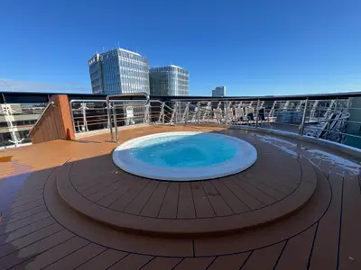Ein runder Whirlpool auf dem Außendeck an Bord der MSC Preziosa mit Blick auf moderne Hochhäuser unter blauem Himmel.