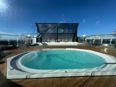 Ein runder Whirlpool mit blauem Wasser auf dem Außendeck an Bord der MSC Preziosa unter strahlend blauem Himmel.