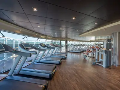 Blick in das helle Fitnessstudio an Bord der MSC Preziosa. Zahlreiche Laufbänder und Krafttrainingsgeräte stehen bereit, mit großen Fenstern zum Meer.