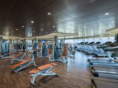 Modernes Fitnessstudio an Bord der MSC Preziosa mit vielen Laufbändern und Kraftgeräten. Große Fenster bieten einen weiten Blick auf das offene Meer. Der helle Raum ist menschenleer.
