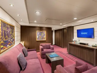 Wohnbereich einer luxuriösen Suite an Bord der MSC Preziosa. Rotes Sofa, Sessel, Couchtisch, TV-Möbel und Kunstwerke schmücken den eleganten Raum.
