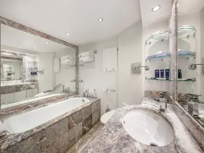 Luxuriöses Badezimmer an Bord der MSC Preziosa mit Marmorverkleidung, Badewanne, Waschbecken und großem Spiegel. Pflegeprodukte und weiße Handtücher sind bereitgelegt.