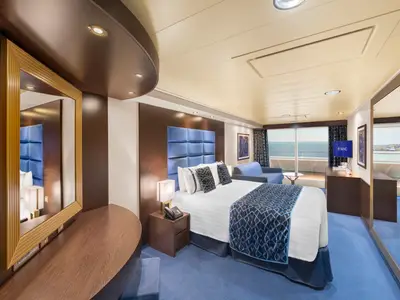 Elegante Premium Suite Aurea an Bord der MSC Preziosa mit Doppelbett, Sofa, TV und Meerblick. Moderne Einrichtung mit blauen Akzenten und dunklen Holzmöbeln.
