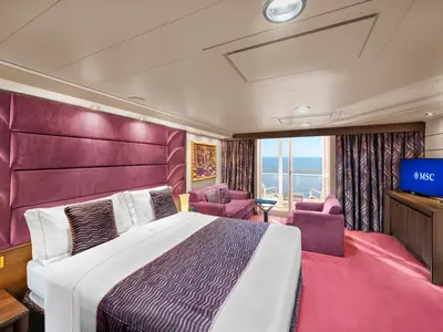 Ein luxuriöses Schlafzimmer an Bord der MSC Preziosa mit einem Doppelbett, einem großen Kopfteil in Purpur, einer Sitzecke mit zwei violetten Sofas und einem Balkon mit Meerblick.