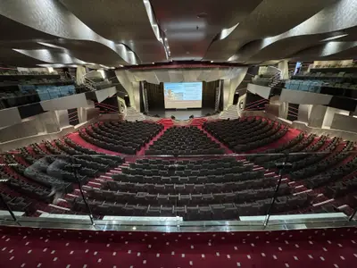 Blick in das große, moderne Theater an Bord der MSC Preziosa mit halbrunden Sitzreihen und einer hell erleuchteten Bühne im Hintergrund.