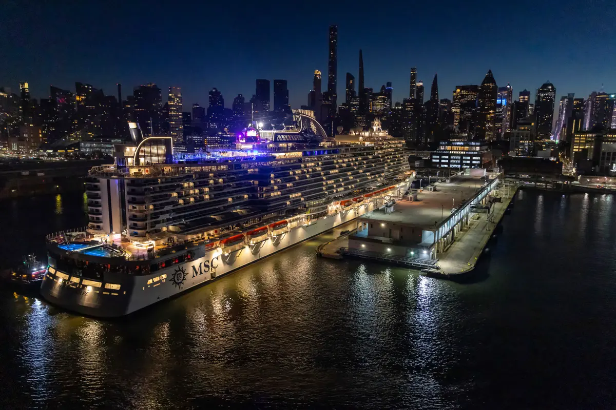 Die MSC Seascape liegt nachts im Hafen von New York City, umgeben von dunklem Wasser und der hell erleuchteten Skyline. Das riesige Schiff ist voll beleuchtet.
