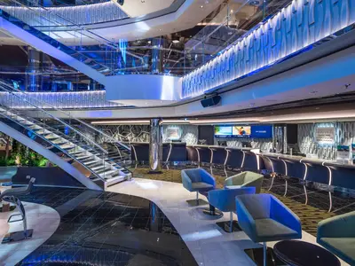 Elegantes Atrium an Bord der MSC Seascape mit beleuchteter Rezeption, grosser Treppe und modernen Sesseln. Blaue Lichtakzente betonen das stilvolle Ambiente.