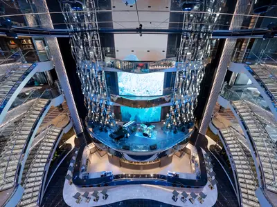 Blick von oben in das beeindruckende, mehrstufige Atrium der MSC Seascape. Es zeigt eine zentrale Buehne mit Musikinstrumenten, darunterliegende Bars und die funkelnden Swarovski-Treppen.