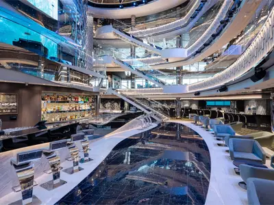 Die Seascape Bar im modernen Atrium der MSC Seascape. Glänzende Bartheke, moderne Barhocker und Lounge-Sessel. Geschwungene Treppen und ein großer LED-Bildschirm bestimmen das futuristische, mehrstöckige Design.