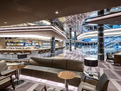 Elegante Shine Bar an Bord der MSC Seascape. Langer Bartresen, Sitzgruppen. Modernes Design mit reflektierenden Oberflächen und indirekter Beleuchtung. Rolltreppen im Hintergrund.