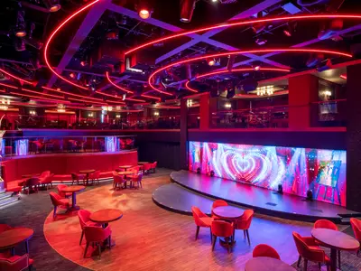 Blick in Le Cabaret Rouge an Bord der MSC Seascape. Ein mehrstöckiger Raum mit roten Sitzgelegenheiten, Tischen und einer Bühne mit großem LED-Bildschirm. Rote Neonlichter betonen die Deckenstruktur und die Ebenen, die für Unterhaltung und Nachtleben konzipiert sind.