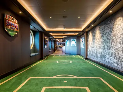 Sportlich gestalteter Korridor an Bord der MSC Seascape. Der gruene Teppichboden ist als Fussballfeld markiert. Links ein 'Sports Bar'-Schild und Bullaugen, rechts eine Wandmalerei jubelnder Fans.