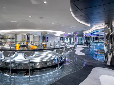 Blick auf die leere Champagne & Wine Bar an Bord der MSC Seascape. Eine geschwungene Bar mit Hochstühlen und Flaschen in Eiskübeln ist zentral. Moderne Beleuchtung und glänzende Oberflächen dominieren den Raum.