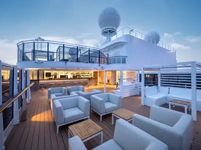Die beleuchtete Top 19 Bar auf dem Sonnendeck der MSC Seascape bei Abendstimmung. Moderne Sessel und Tische stehen bereit. Eine gut bestückte Bar mit warmer Beleuchtung schafft entspannte Atmosphäre an Bord.